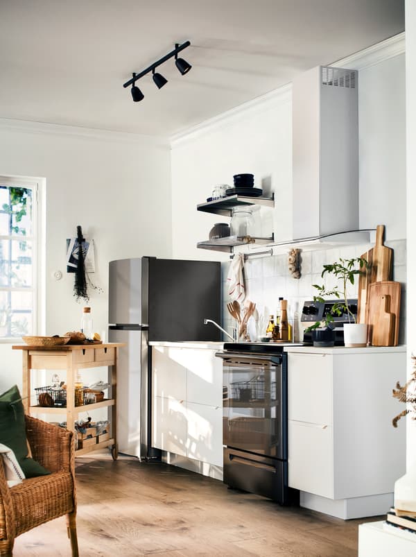 Une cuisine en noir et blanc avec des tons chaleureux de bois provenant du plancher, du comptoir et de la desserte sur roulettes en bois FÖRHÖJA.
