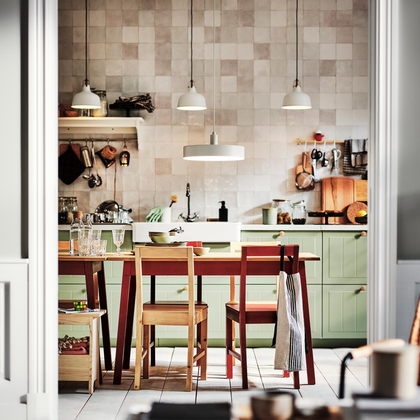 Une cuisine équipée de façades de tiroirs STENSUND vert clair et de deux tables PINNTORP entourées de chaises PINNTORP.