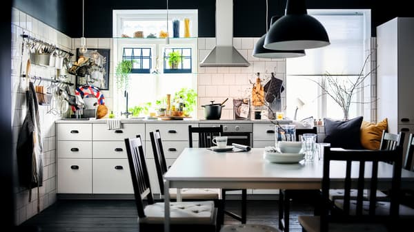 Une cuisine noir et blanc avec des rangements METOD blancs avec des intérieurs MAXIMERA et un espace salle à manger avec deux tables MELLTORP blanches.