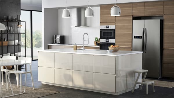 Une cuisine ouverte avec un îlot de cuisine ainsi qu’une combinaison de façades beige clair brillant et à effet noyer, une table et des chaises.