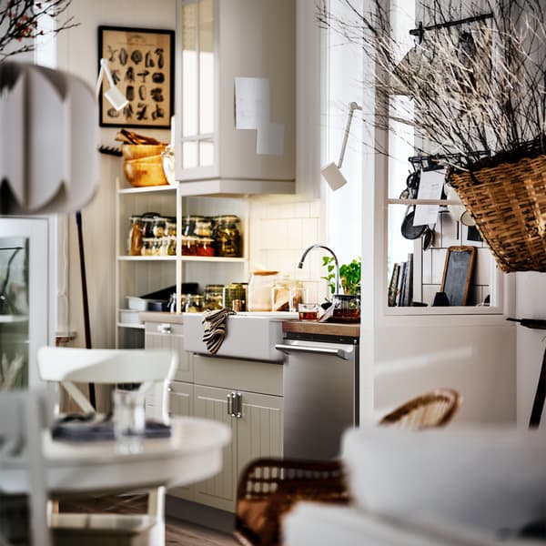 Une cuisine STENSUND au style rustique blanc-beige avec un évier HAVSEN et des étagères ouvertes et fermées contenant des bocaux et une batterie de cuisine.
