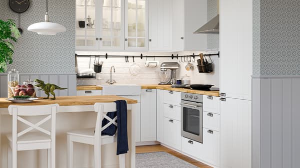 Une cuisine STENSUND blanche de style traditionnel avec des portes en bois, du papier peint fleuri, un îlot de cuisine et deux tabourets de bar.