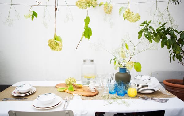 Une déco de table avec de la vaisselle à motif, des verres et un vase de fleurs au dessus de laquelle sont suspendues des fleurs.