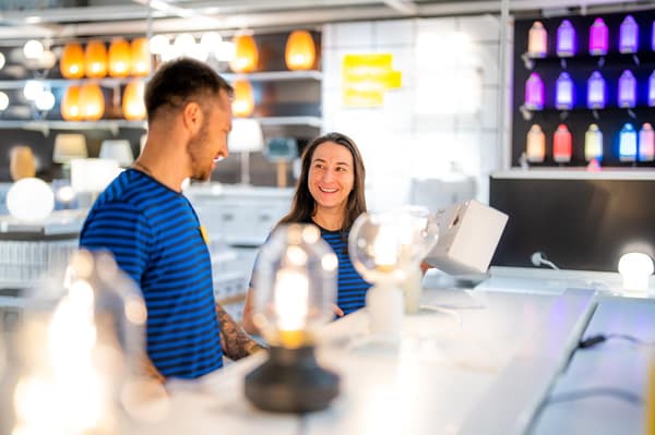 Une employée IKEA en chemise jaune scelle un colis avec un pistolet à colle chaude.