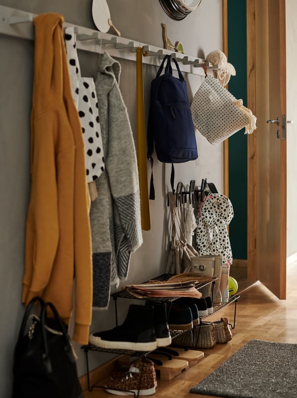 Une entrée avec trois étagères à chaussures GREJIG noires, des manteaux et des sacs suspendus à deux patères KUBBIS blanches dotées d’une rangée de sept crochets.
