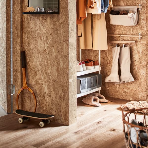 Une entrée avec un rangement ouvert pour vêtements et chaussures, un panier en rotin contenant des chaussures et une barre supportant des bottes sur un porte-jupe.