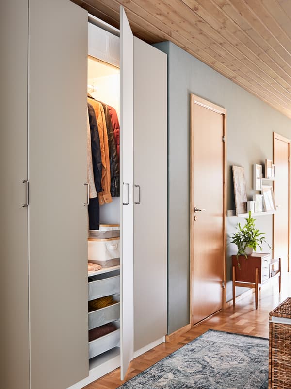 Une entrée étroite avec une armoire-penderie PAX blanche, des étagères, des tiroirs et des portes.
