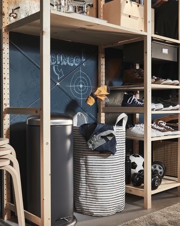 Une étagère en bois dans laquelle un grand trou accueille une poubelle et un sac à linge, une cible est dessinée au-dessus.