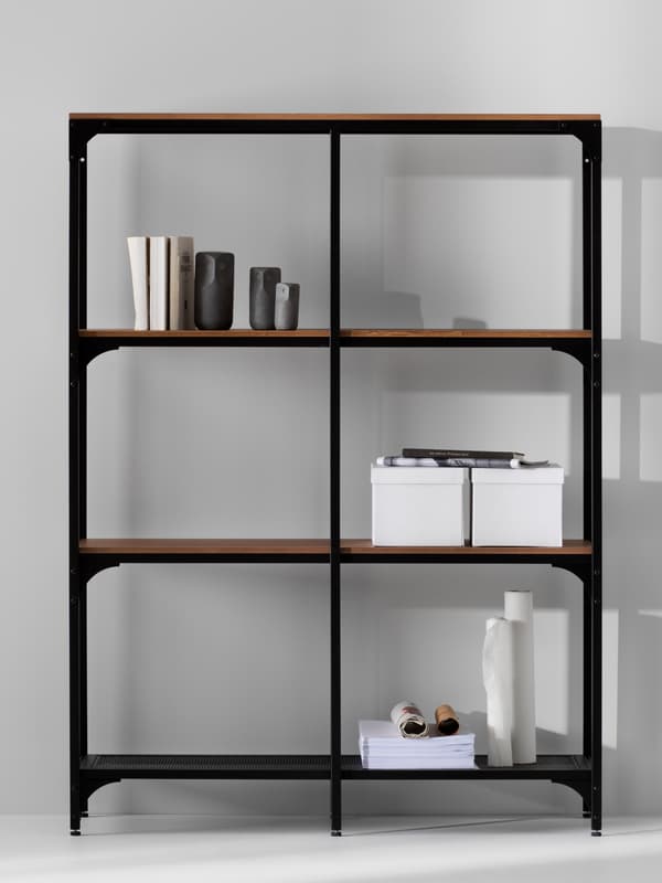 Une étagère FJÄLLBO noire contre un mur gris. Sur les tablettes se trouvent deux boîtes, quelques livres et une collection de bibelots.