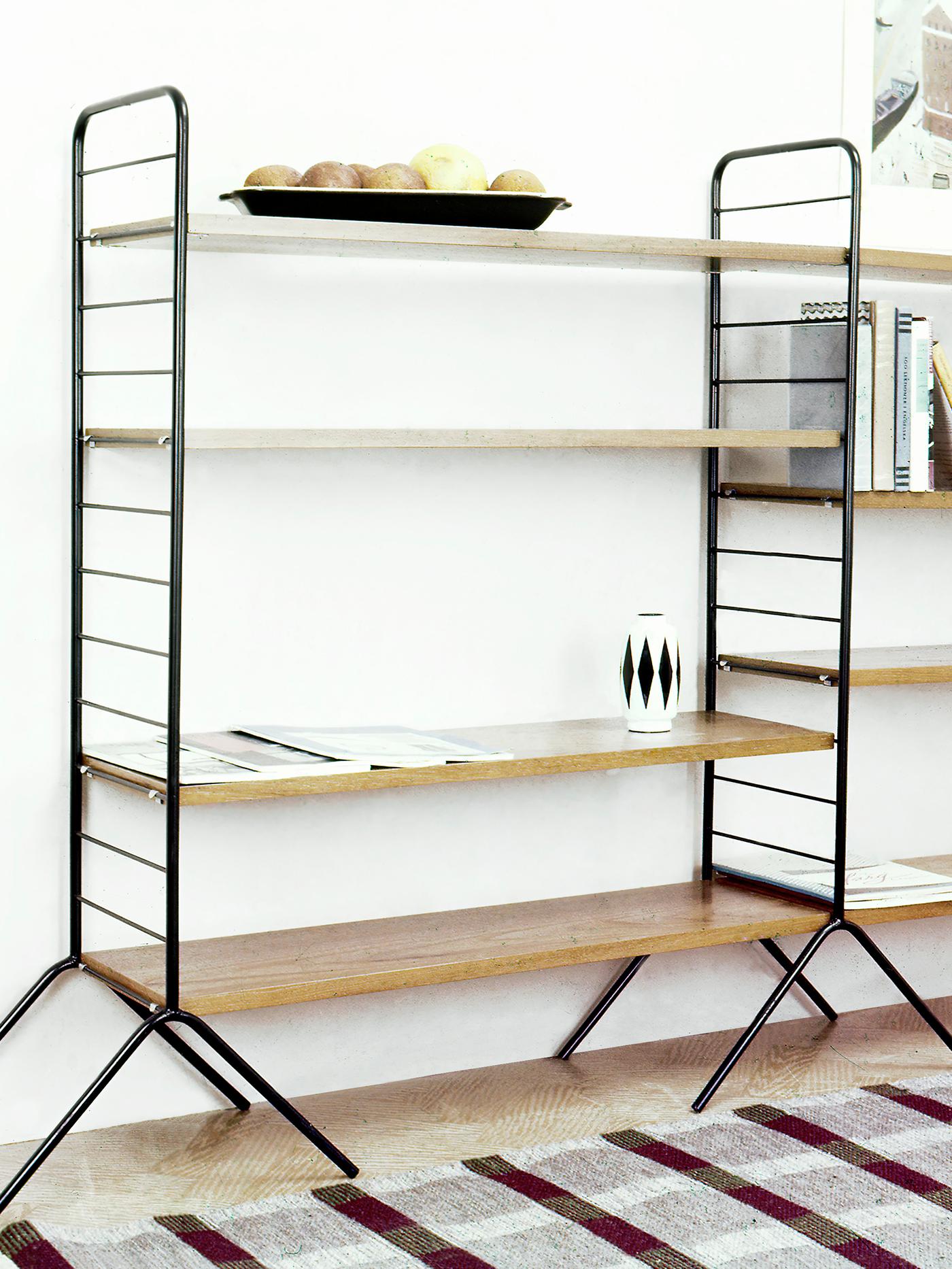 Une étagère IKEA HANSA de 1957 composée de montants et pieds en métal noir, avec des étagères en bois.