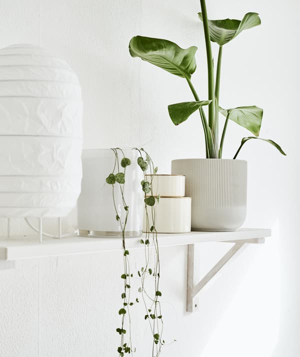 Une étagère murale blanche sur laquelle se trouvent une lampe blanche, des cache-pots et des décorations.