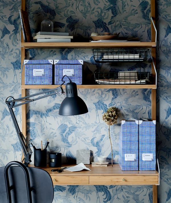 Une étagère murale qui sert en même temps de petit bureau à domicile; différents rangements, une lampe de bureau, une chaise de bureau et du papier peint à motifs.