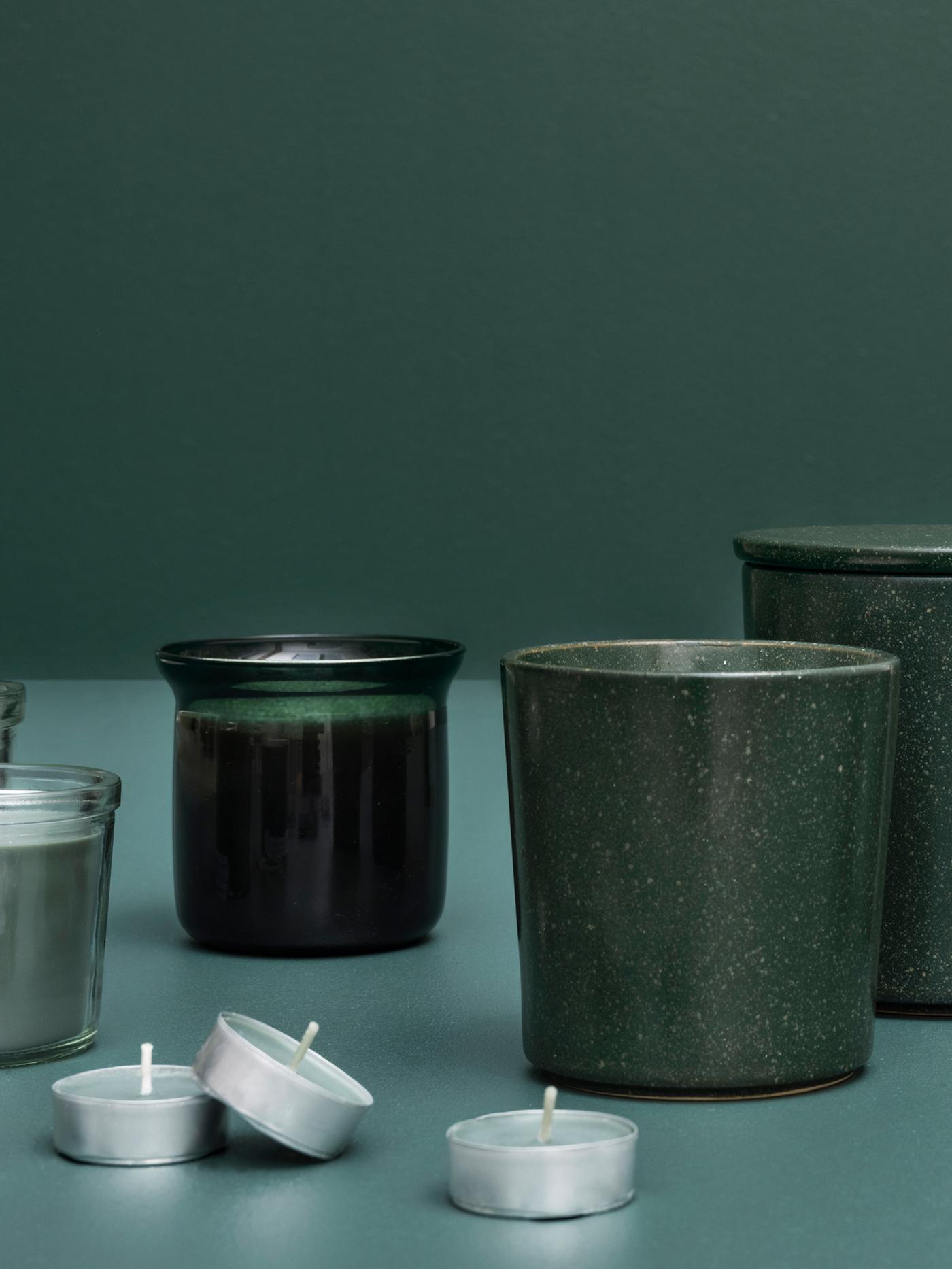Une exposition artistique de plusieurs bougies parfumées à la menthe AVMÅLA dans des contenants différents contre un fond vert foncé.