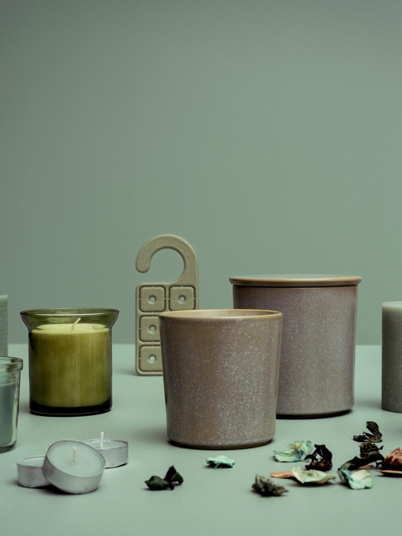 Une exposition de plusieurs bougies parfumées à l'herbe fraîche HEDERSAM, du potpourri et un cintre parfumé contre un fond vert.