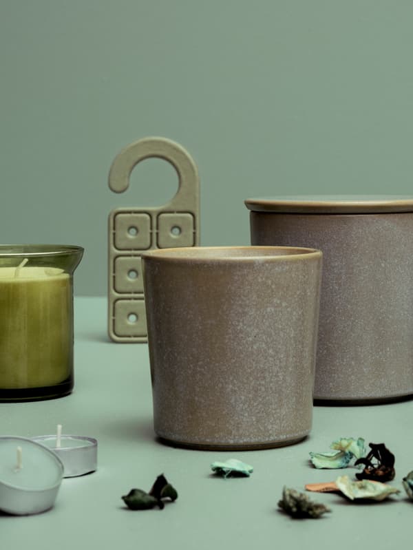 Une exposition de plusieurs bougies parfumées à l’herbe fraîche HEDERSAM, du pot-pourri et un cintre parfumé contre un fond vert.
