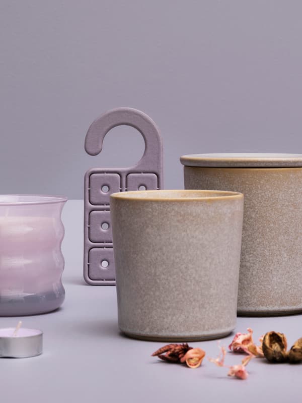 Une exposition de plusieurs bougies parfumées au pois sucré JÄMNMOD, du pot-pourri et un cintre parfumé contre un fond violet.