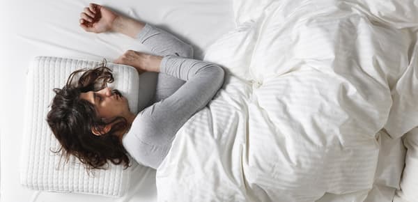 Une femme allongée sous la couette sur le côté sur un oreiller ergonomique