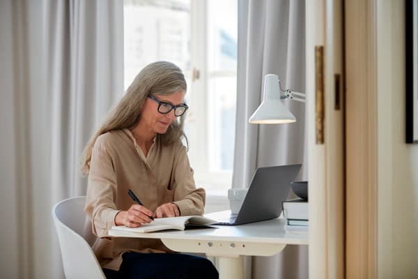 Une femme aux long cheveux et portant des lunnettes travaillant sur un bureau devant un ordinateur portable