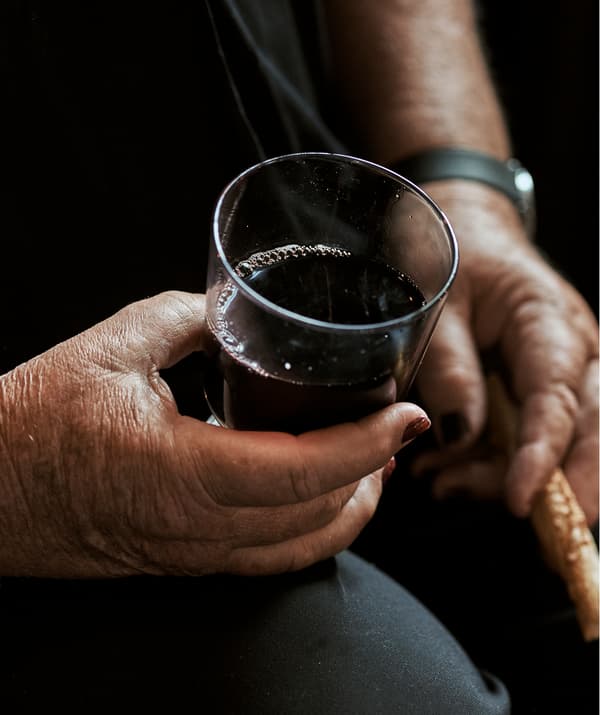 Une femme aux ongles manucurés est assise et tient un verre de vin dans une main et un gressin dans l’autre.