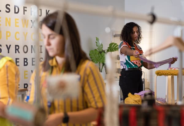 Une femme avec un haut à motifs découpe des bandes de tissu violet pour couvrir une chaise en bois. Un collaborateur IKEA travaillant sur un projet de bricolage.