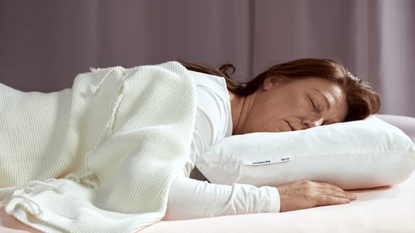 Une femme couchée sur le ventre, la tête posée sur un oreiller de petit volume.