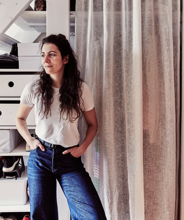 Une femme debout devant un espace de rangement de vêtements caché derrière un rideau.