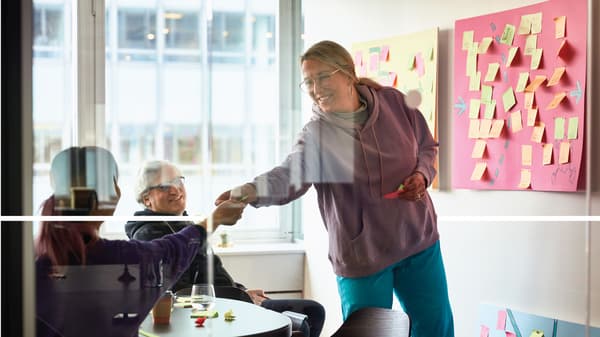 Une femme debout donne un bout de papier à une autre femme assise devant elle