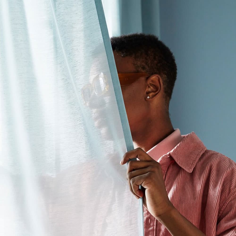 Une femme derrière un voilage bleu clair.