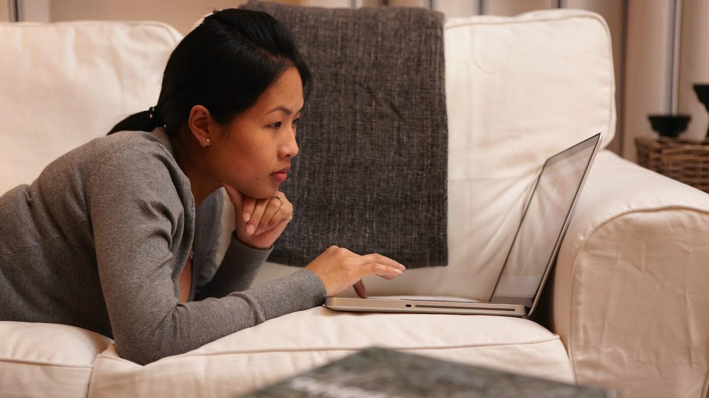 Une femme en train de faire de l'ordinateur allongée sr son canapé