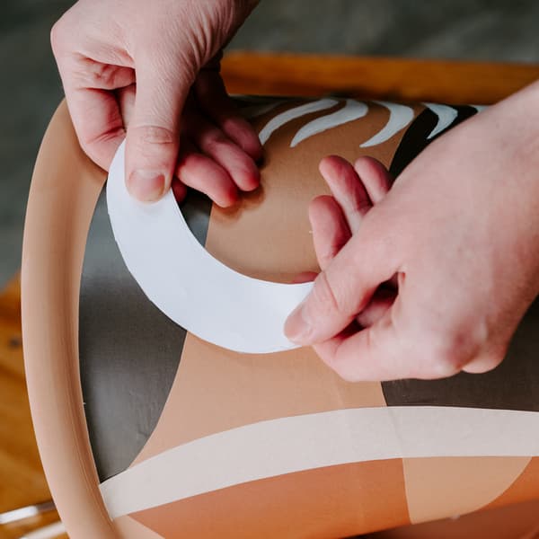 Une femme est en train de customiser un cache pot en terre cuite à l'aide de peinture