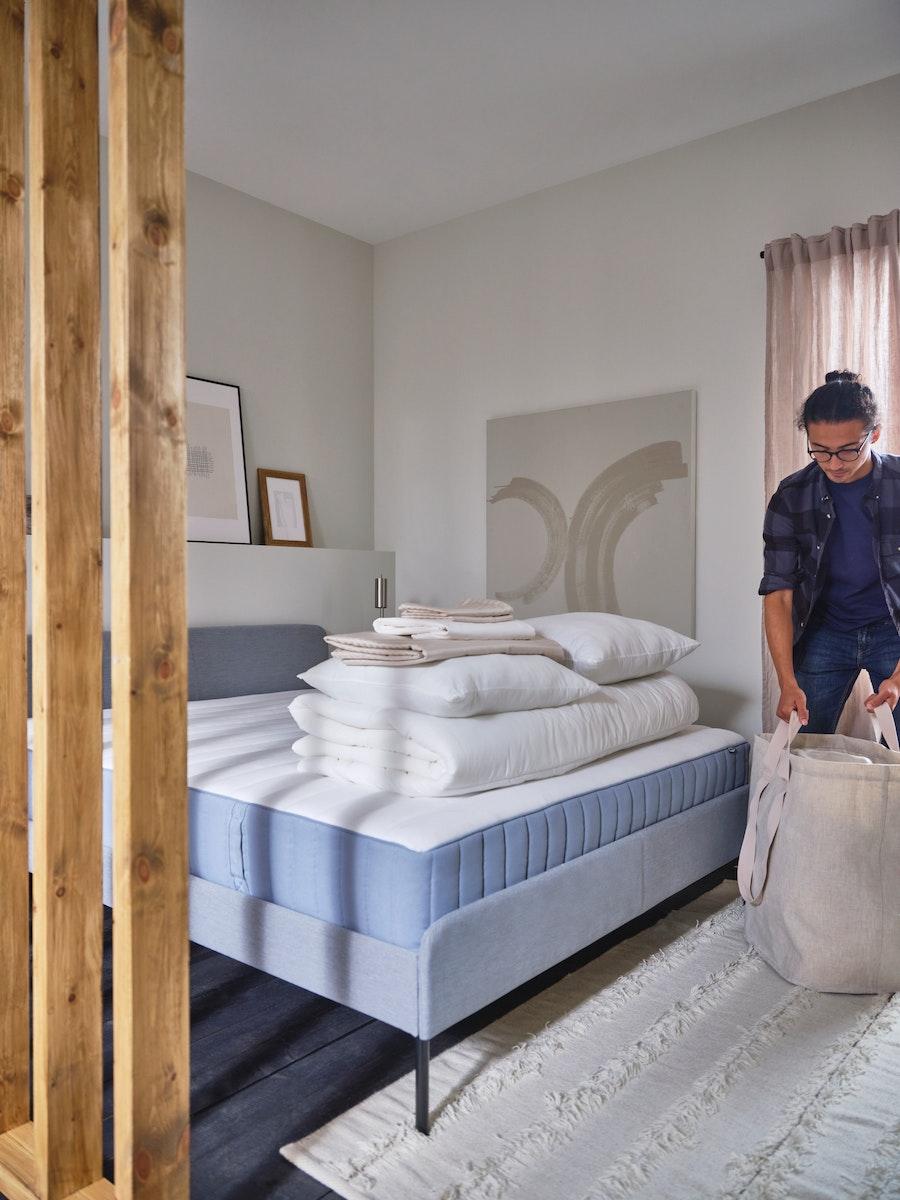 Une femme est en train de déposer des affaires sur un lit pas fait.