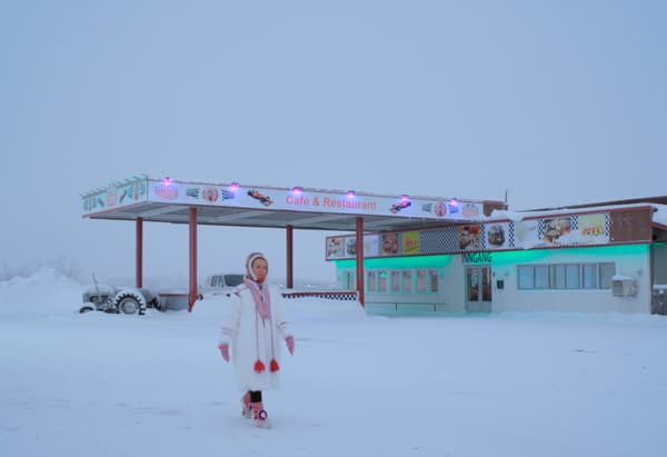 Une femme marchant à travers un paysage enneigé désert avec un restaurant en arrière-plan.