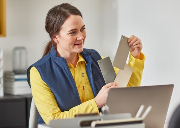 Une femme portant la tenue bleue et jaune des collaborateurs IKEA tient des échantillons de couleur en regardant de l’autre côté de son bureau.