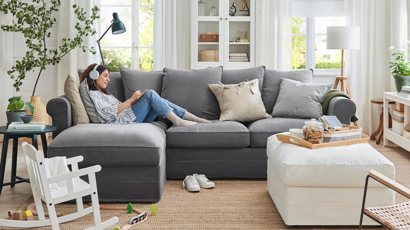 Une femme portant un casque audio se relaxe sur un canapé 3 places GRÖNLID avec méridienne dans un salon familial.