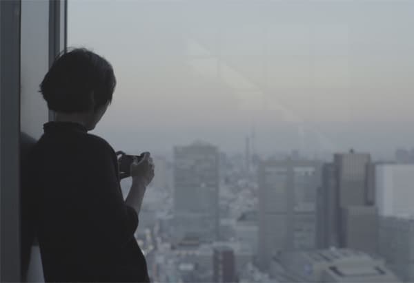 Une femme prenant une photo d’un paysage urbain à travers une fenêtre.