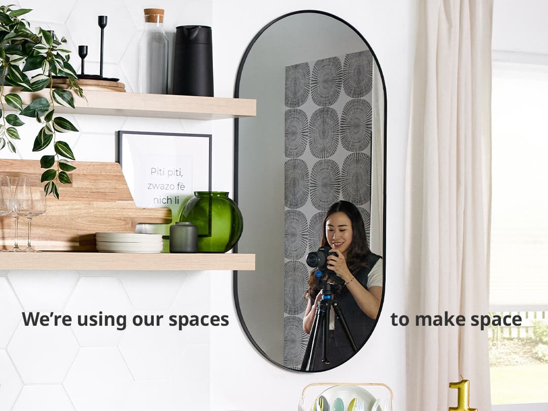 Une femme prend une photo avec un appareil photo, reflétée dans un miroir ovale, dans une cuisine moderne avec des étagères, des décorations et un texte superposé : « Nous utilisons nos espaces pour créer de l'espace. »