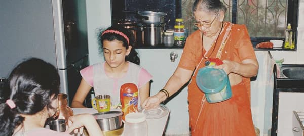 Une femme range les restes, deux jeunes filles sont assises à table.