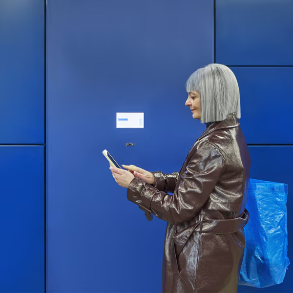 Une femme regarde son téléphone pour récupérer son colis devant lex box de click and collect.