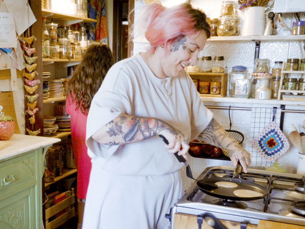 Une femme sourit et prépare des crêpes dans une poêle à crêpes HEMLAGAD sur la cuisinière.
