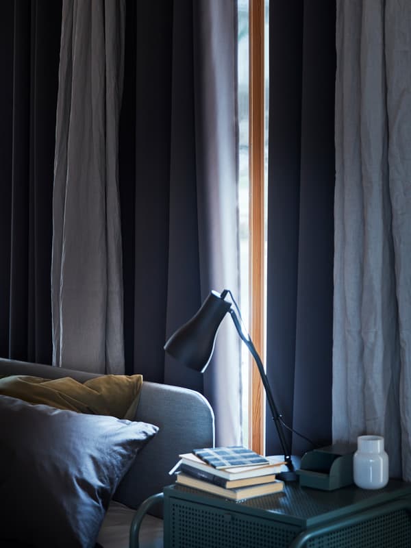 Une fenêtre dans une chambre à coucher bleue, le soleil presque entièrement caché derrière des rideaux occultants HILLEBORG.