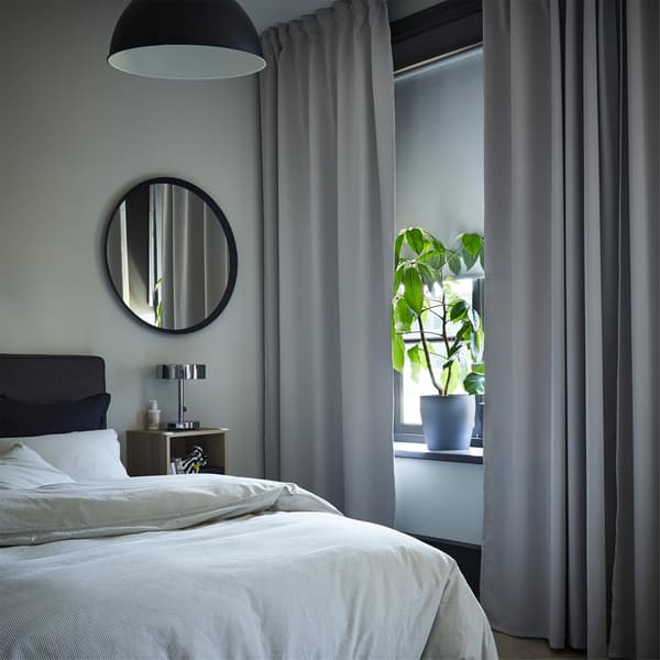 Une fenêtre de chambre à coucher avec des rideaux obscurcissants gris clair et un store occultant blanc qui couvre la moitié de la fenêtre.