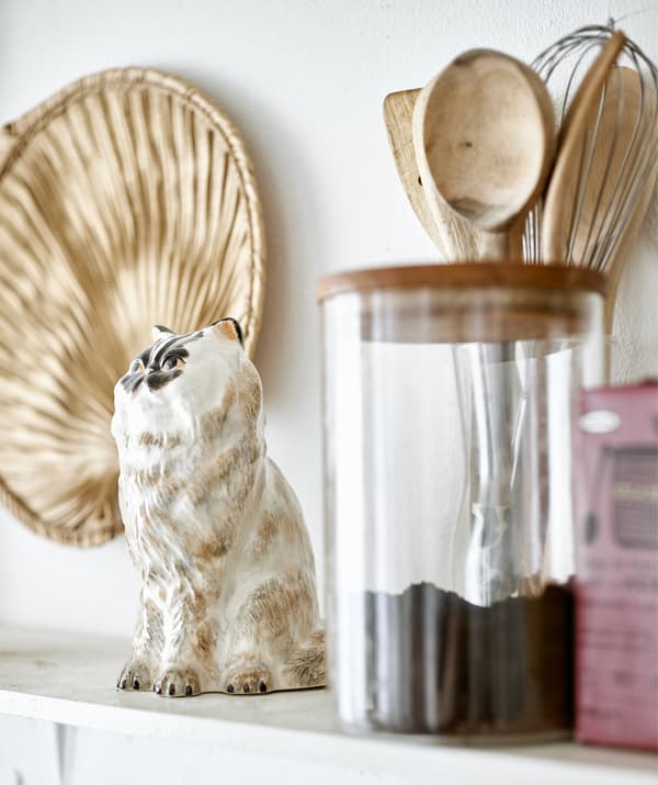 Une figurine de chat, des ustensiles de cuisine en bois et un pot de café sur une étagère de cuisine.