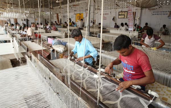 Une grand atelier avec des personnes tissant de la laine sur des métiers.