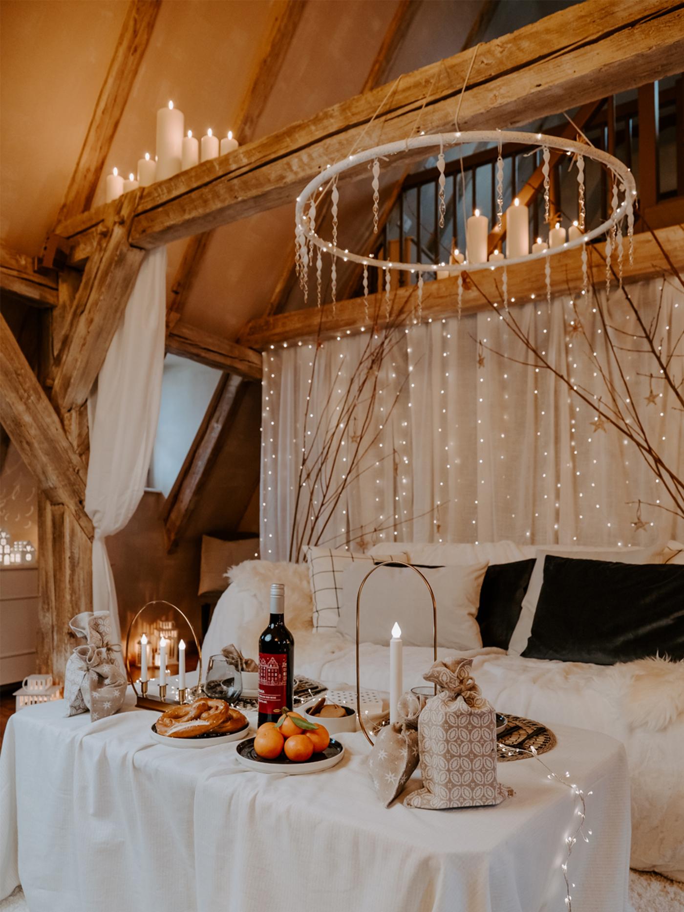 Une grande table avec une nappe blanche devant un canapé blanc et beaucoup de guirlandes lumineuses accrochées au mur et au plafond.