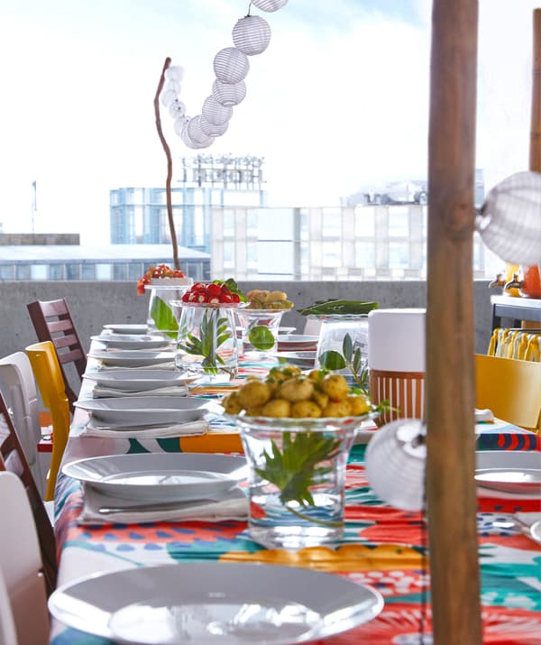 Une guirlande lumineuse à LED IKEA SOLARVET avec douze ampoules à énergie solaire suspendues au-dessus d’une table de fête d’été colorée.
