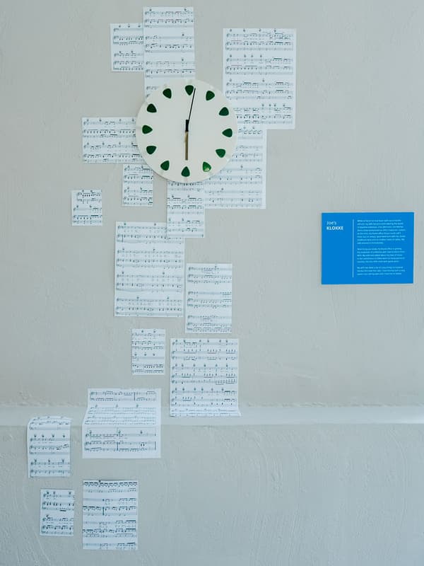 Une horloge murale est en exposition, ainsi que des partitions de musique collées au mur.