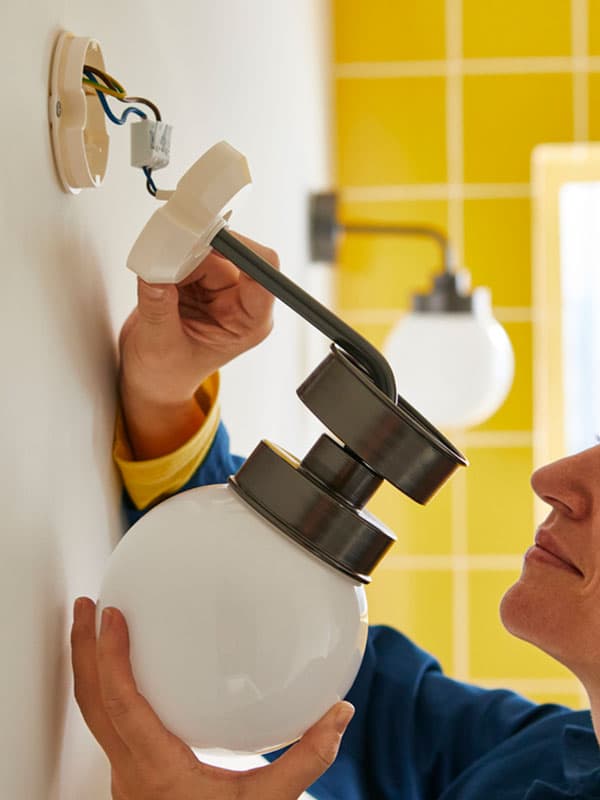 Une installatrice IKEA qui pose un luminaire de salle de bains.