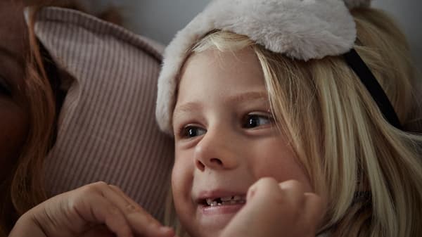 Une jeune enfant aux longs cheveux blonds est allongée sur un oreiller moelleux. Elle porte un masque tout doux sur le visage.