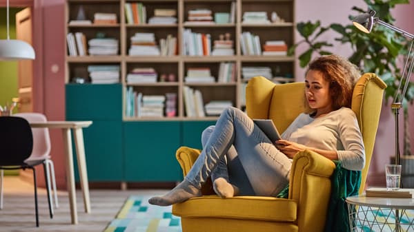 Une jeune femme en train de lire dans un fauteuil STRANDMON jaune.