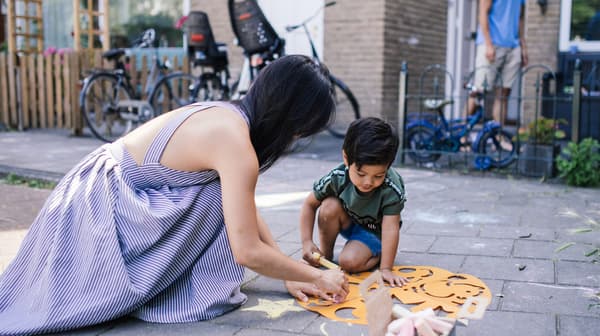 Une jeune femme portant une robe et un petit garçon portant un T-shirt et un short font du bricolage dans la rue devant une maison.